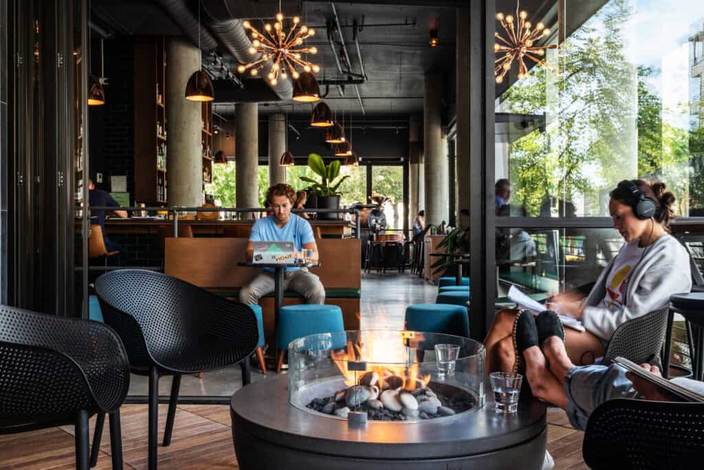 Modern coffee shop interior with seating and fire pit, natural light, and greenery outside.