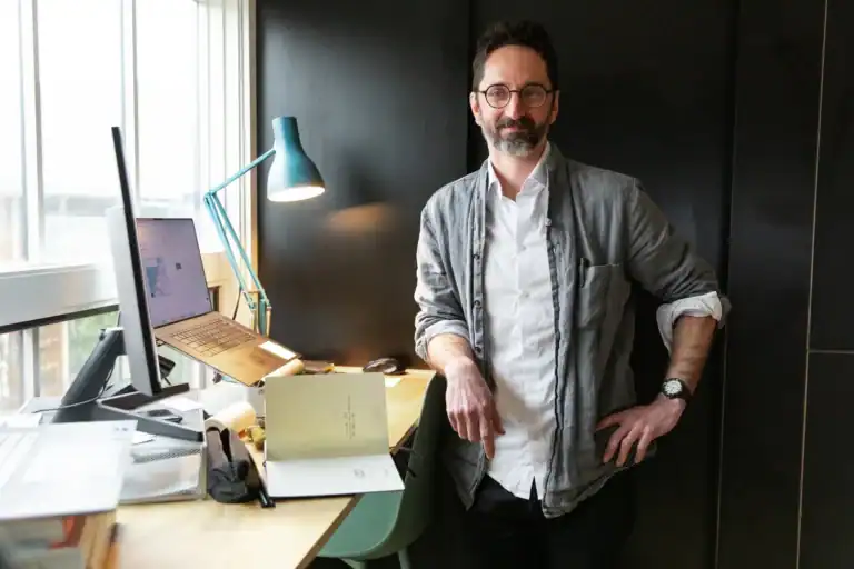 Man standing in modern office with desk and computer setup.
