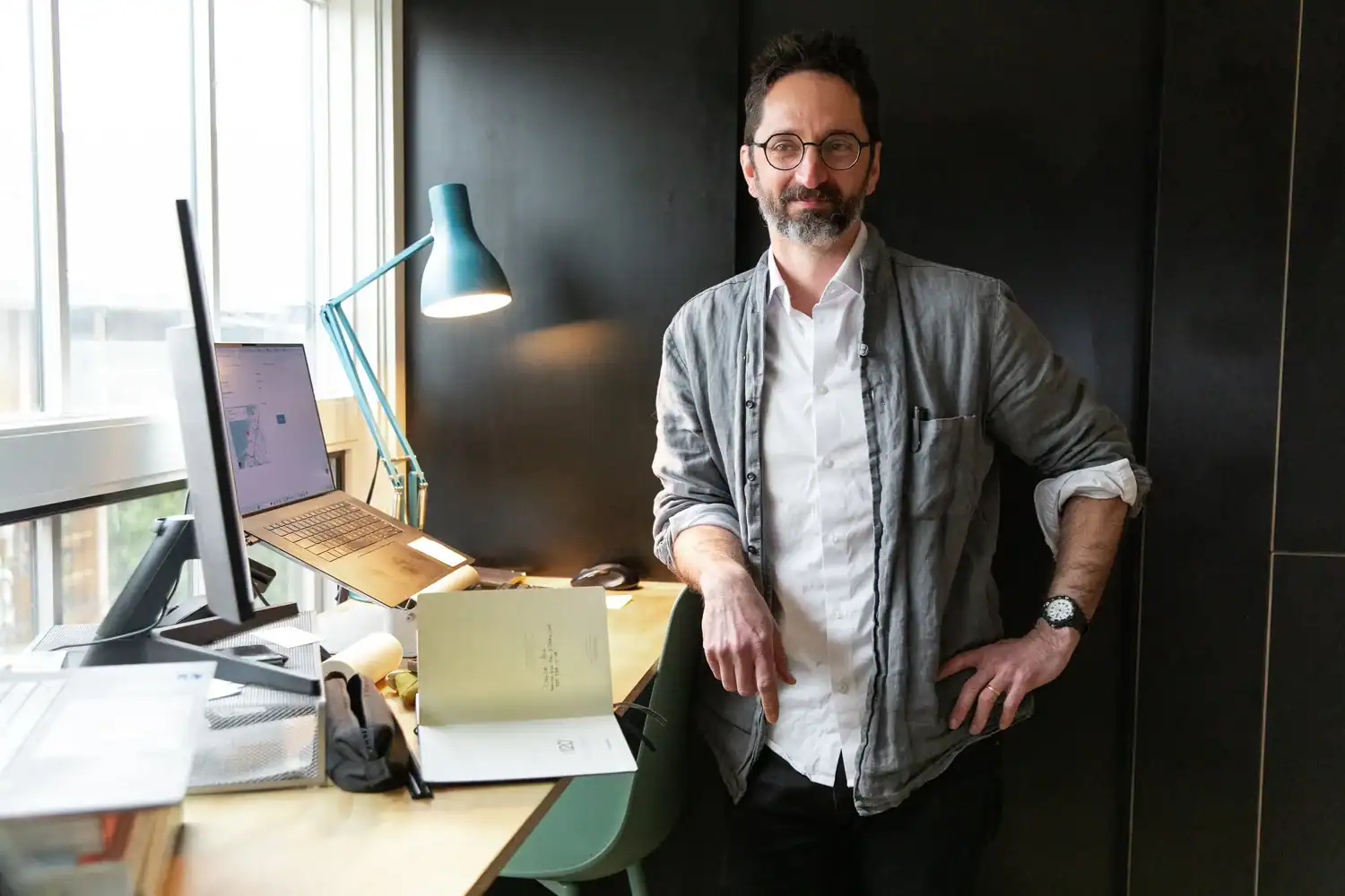 Man standing in modern office with desk and computer setup.