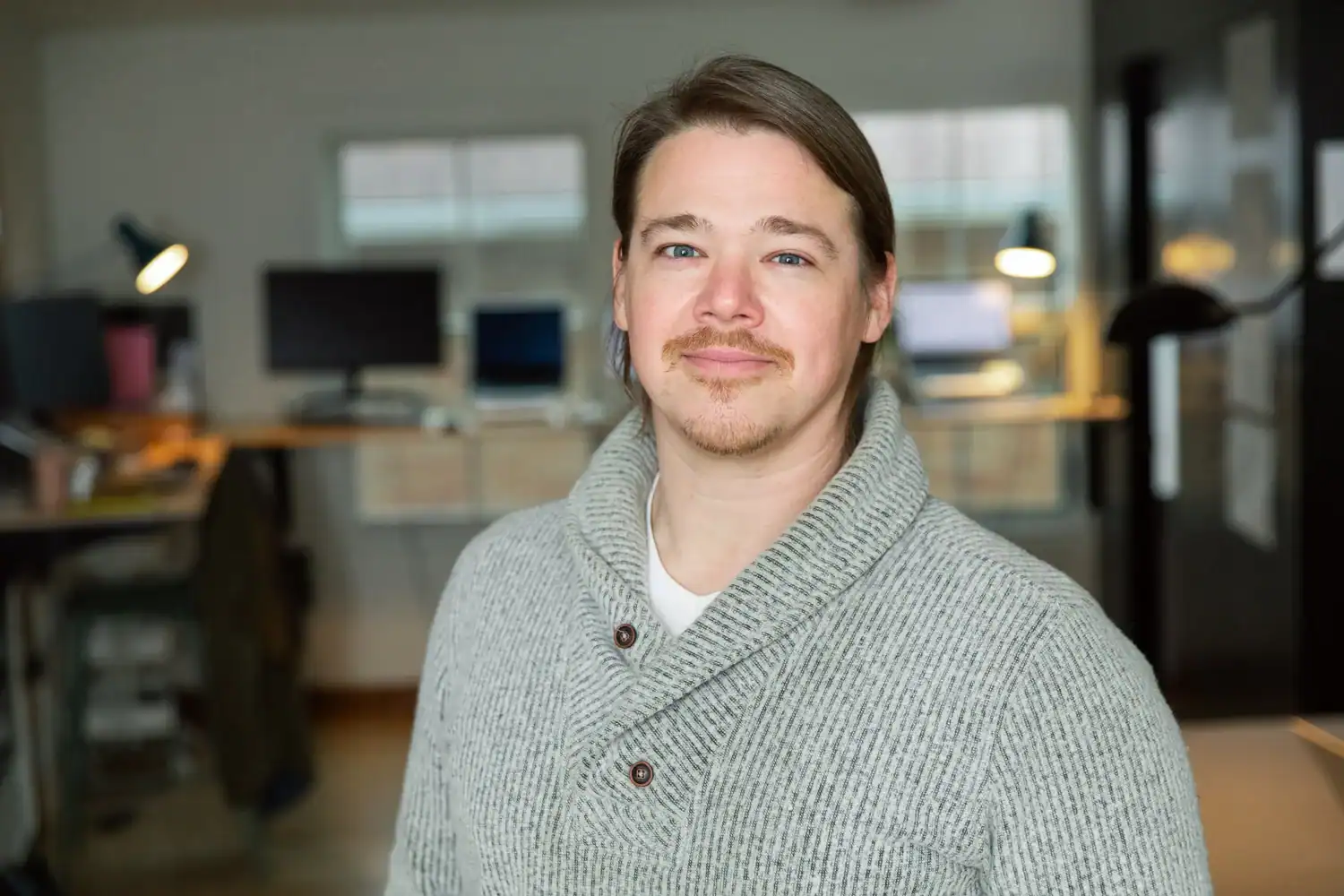 Portrait of a man in a gray sweater in an office environment.