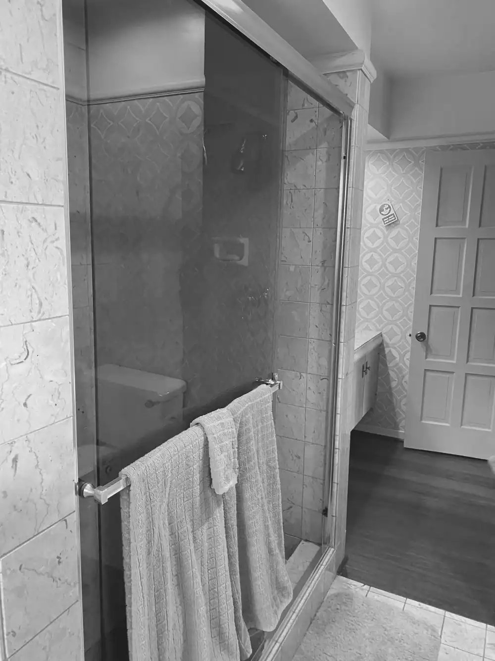 Bathroom shower with glass door and towels, traditional tile design.