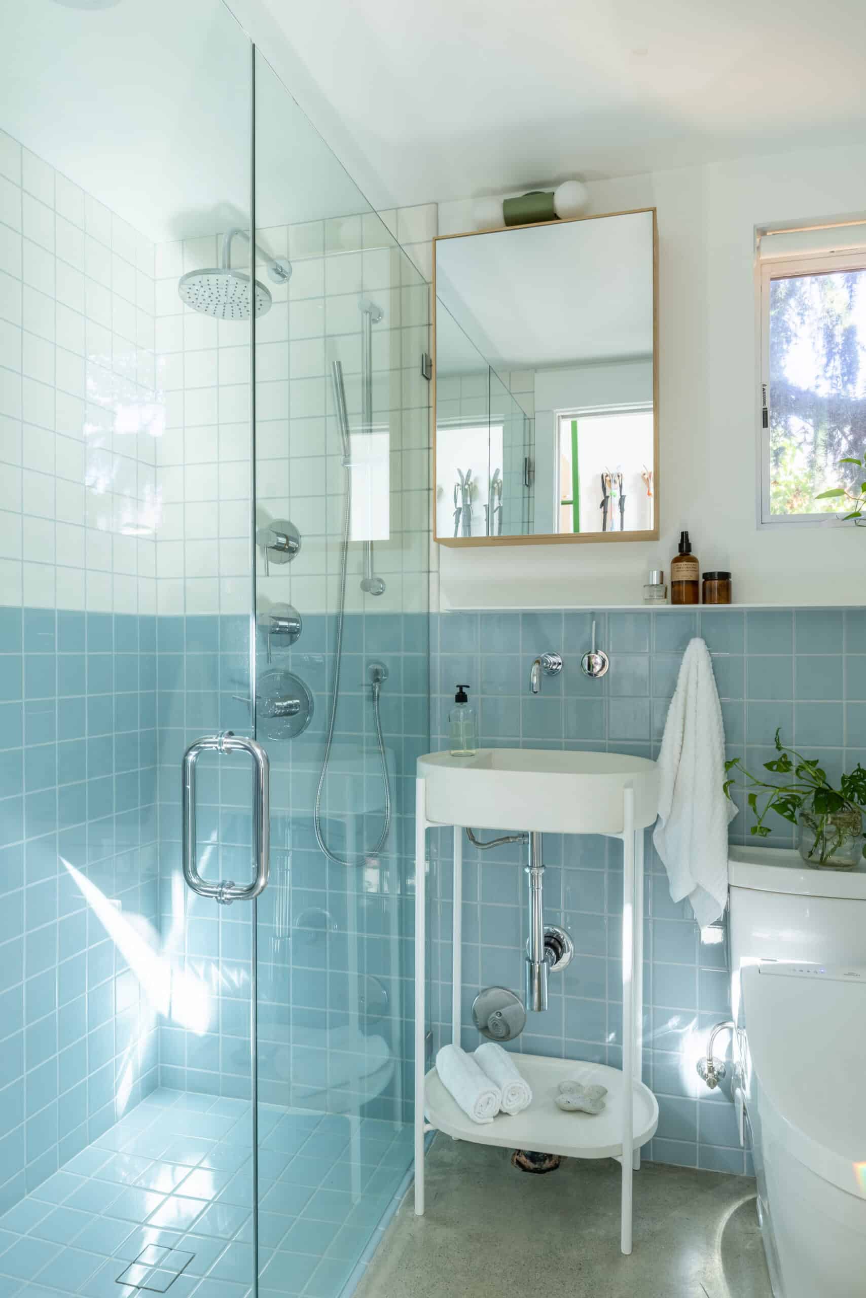 Bright bathroom with blue tiles, glass shower, and white fixtures.