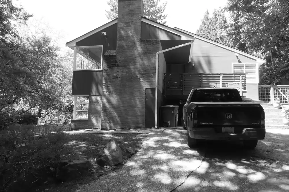Modern residential house with a truck parked in front, surrounded by trees.