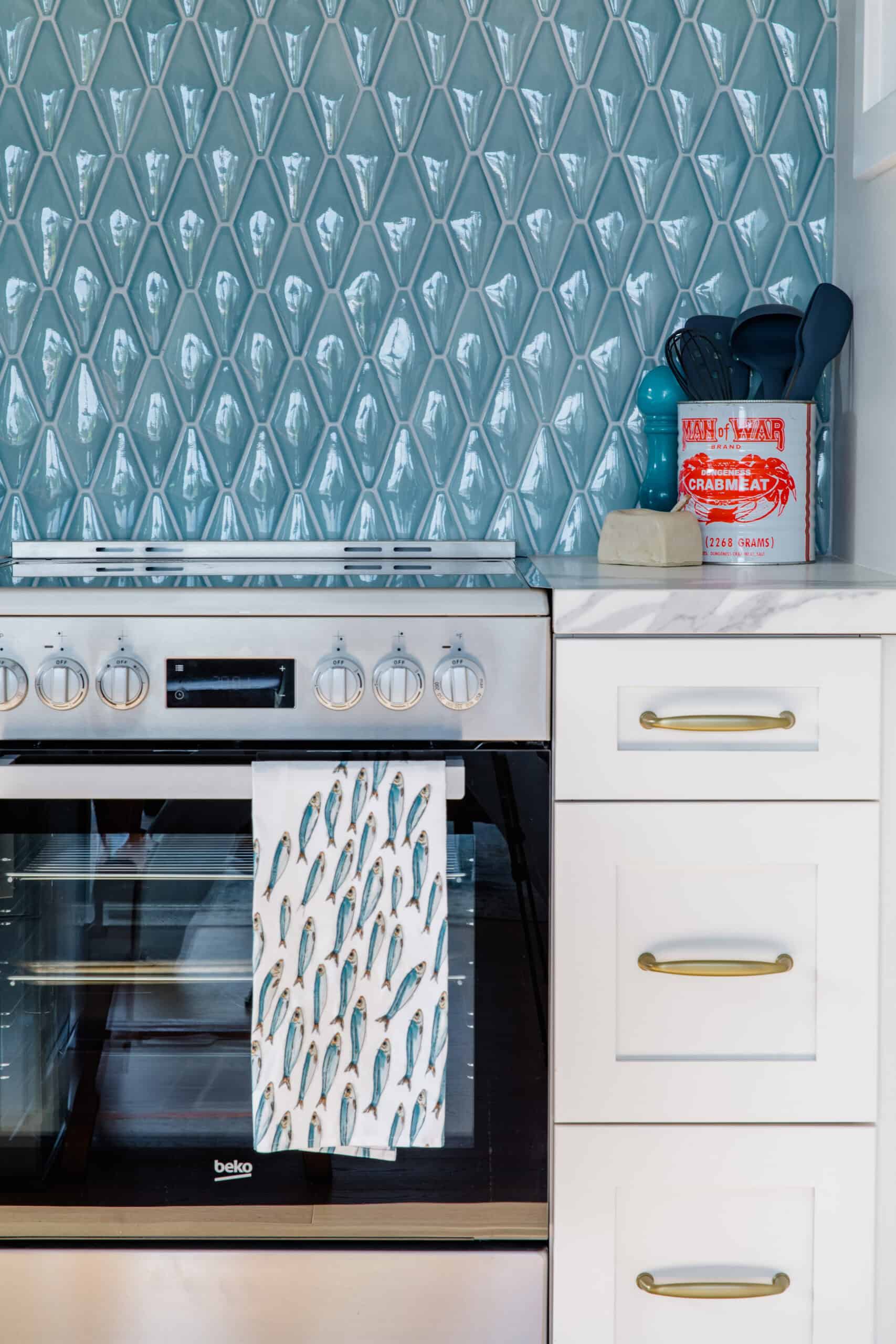 Modern kitchen with teal geometric tile backsplash and white cabinetry.