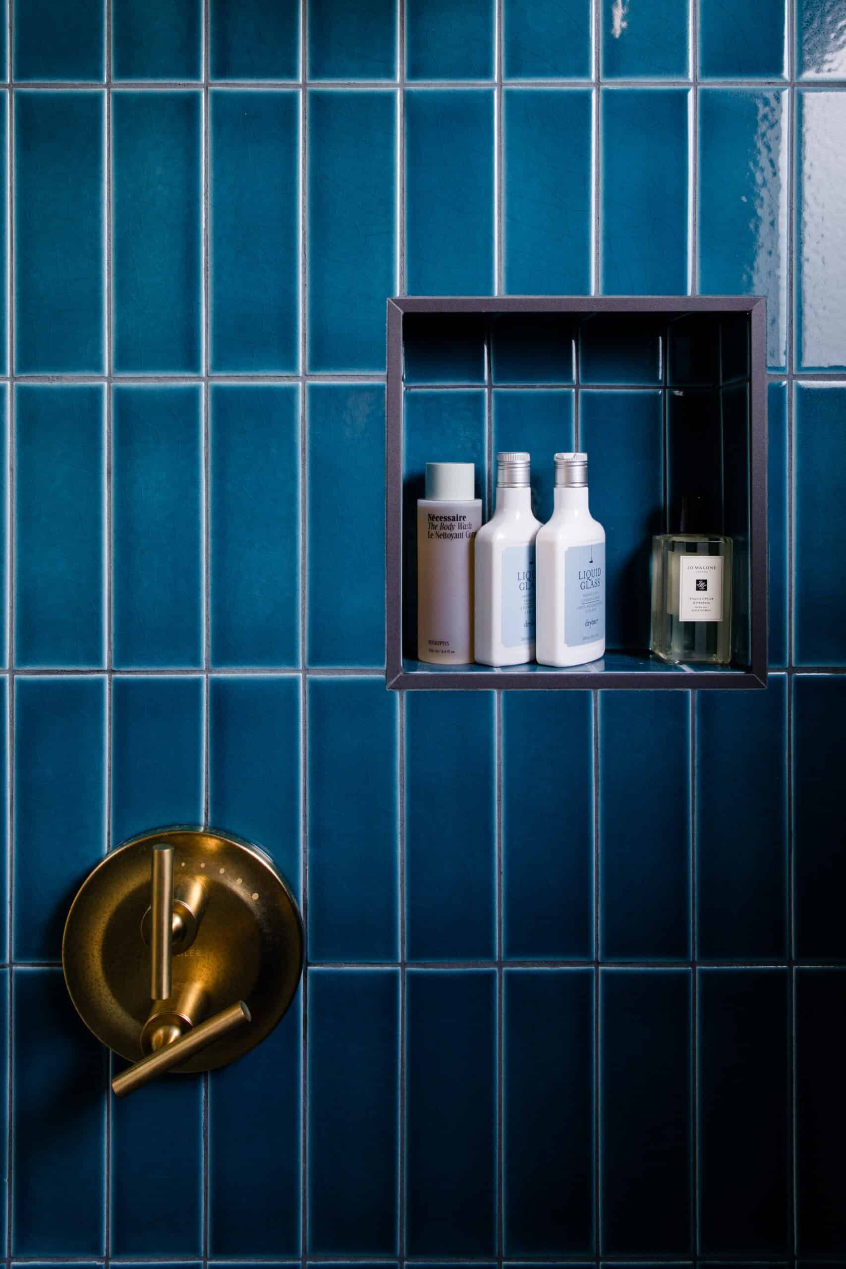 Blue tiled wall with built-in shelf holding toiletries and a brass shower valve.