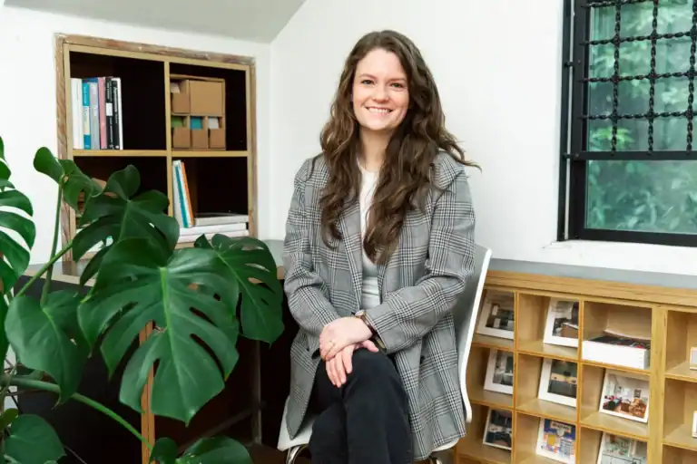 Young woman smiling in modern office space with plants and bookshelves.