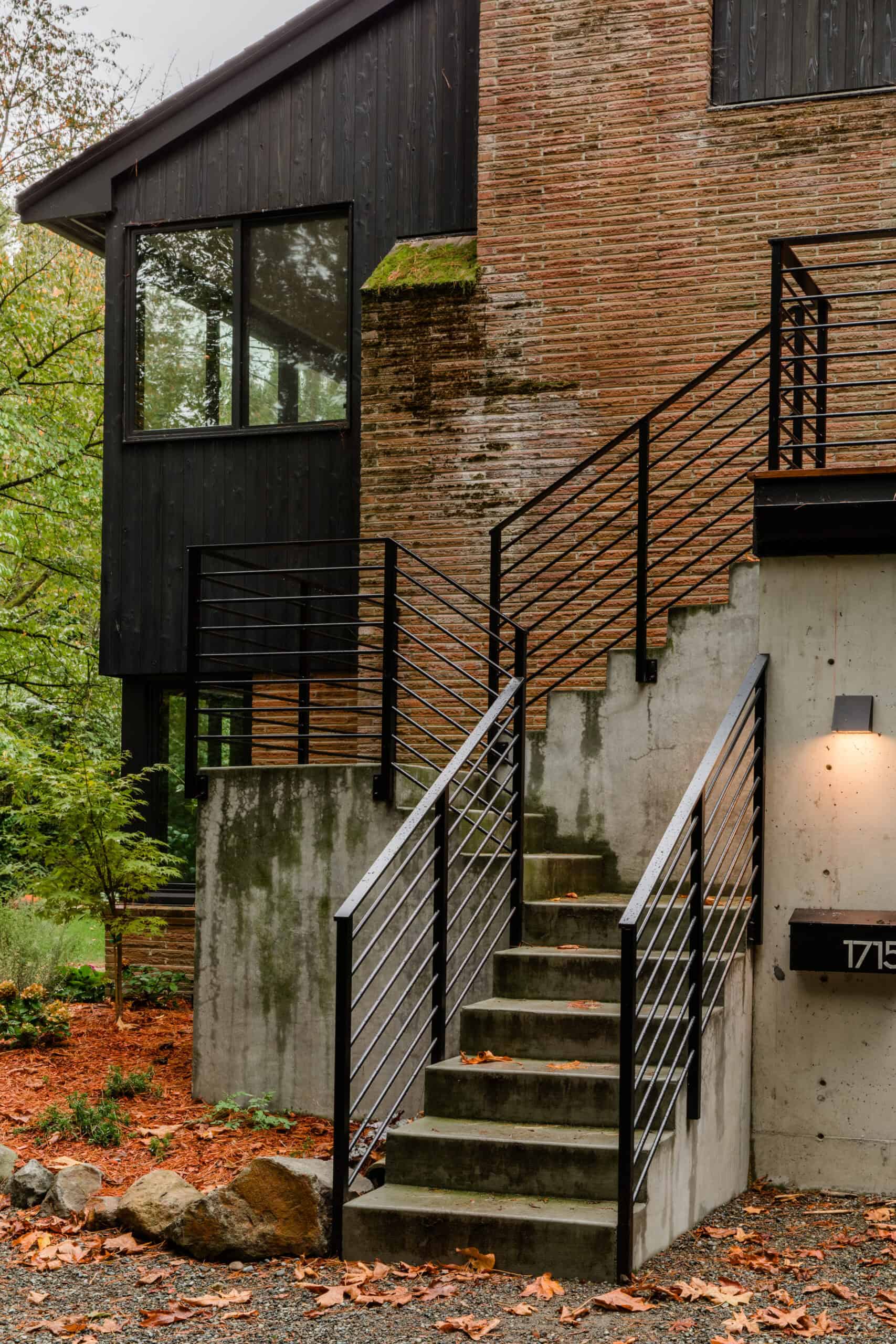 Modern exterior stairs with black metal railing and brick wall.