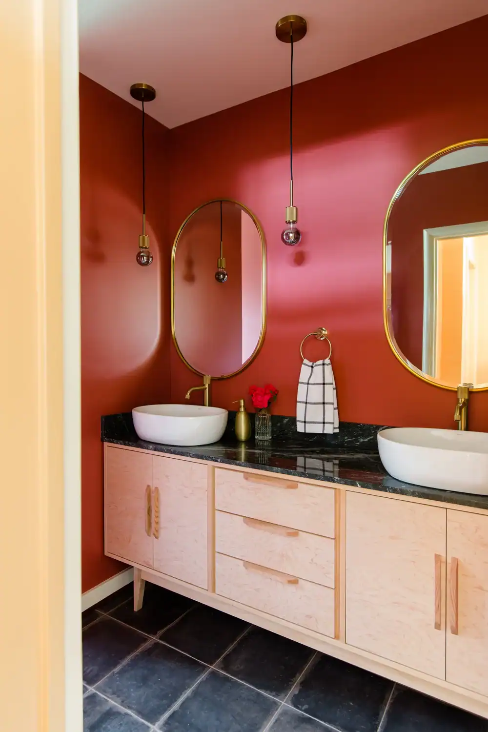 Contemporary bathroom with dual sinks, oval mirrors, and warm wall color.