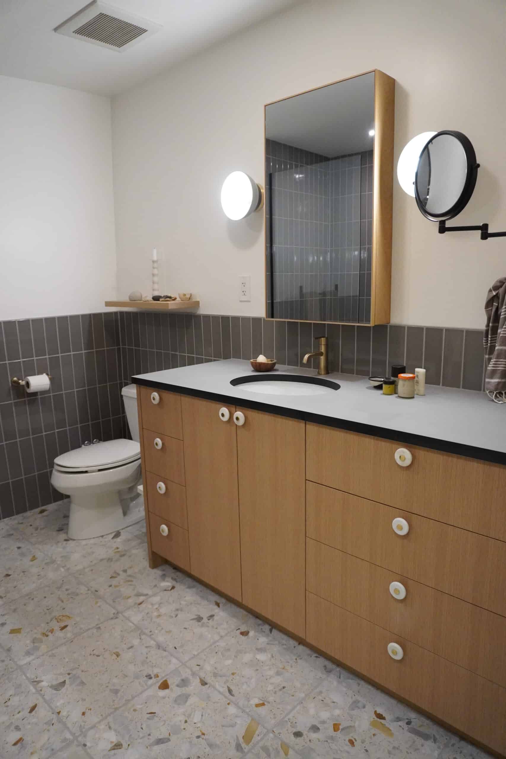 Contemporary bathroom with wooden vanity, mirror, and modern lighting fixtures.