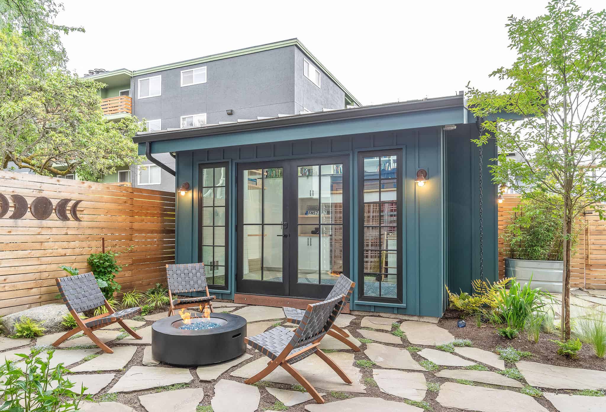 Contemporary backyard office shed with large glass doors and outdoor seating area.