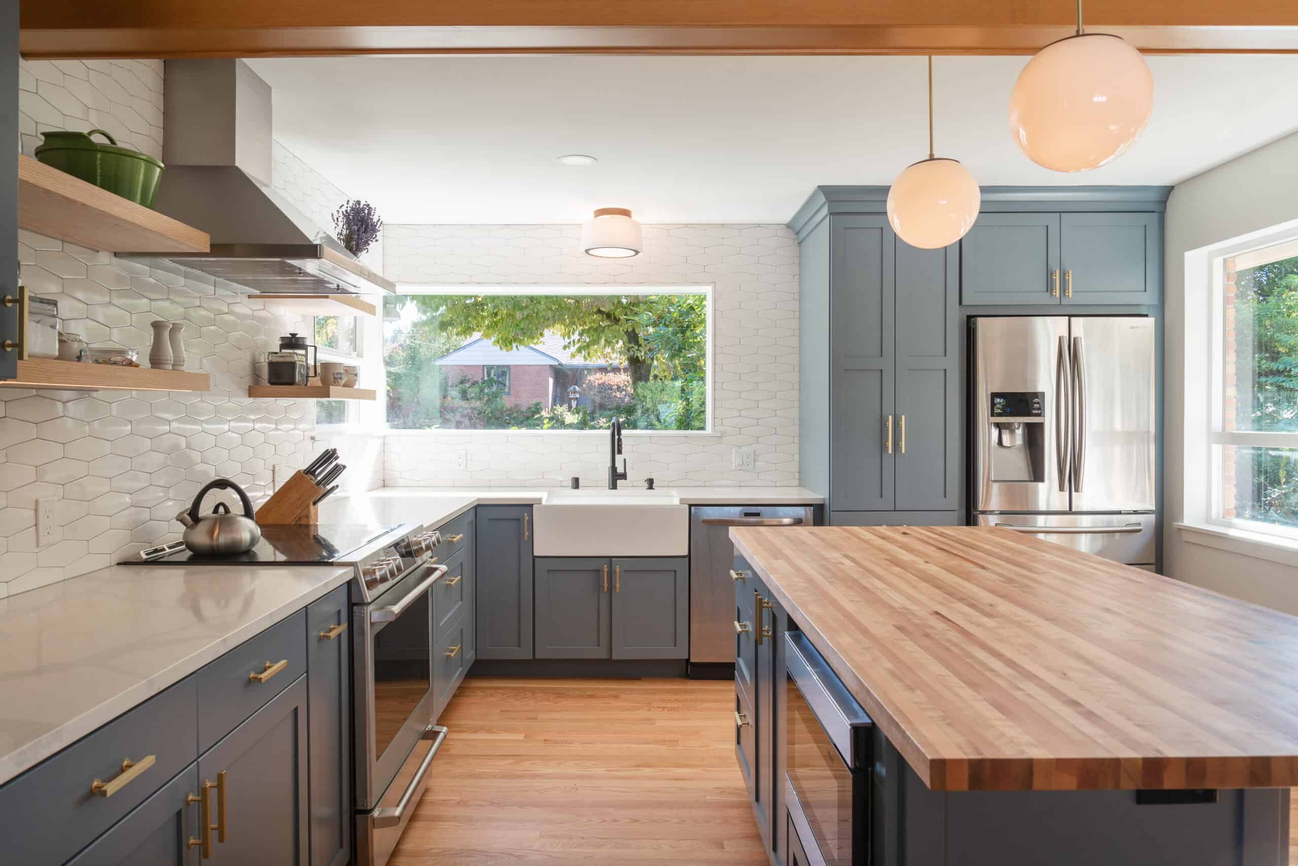 Contemporary kitchen with blue cabinets, wooden island, and large window view.