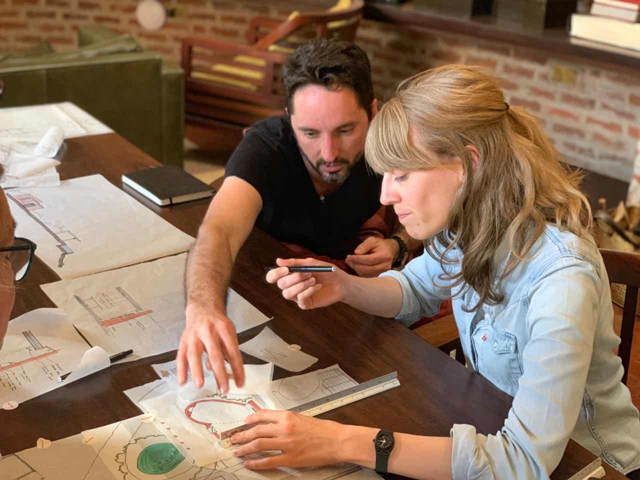 Two architects reviewing blueprints and design plans at a workspace.