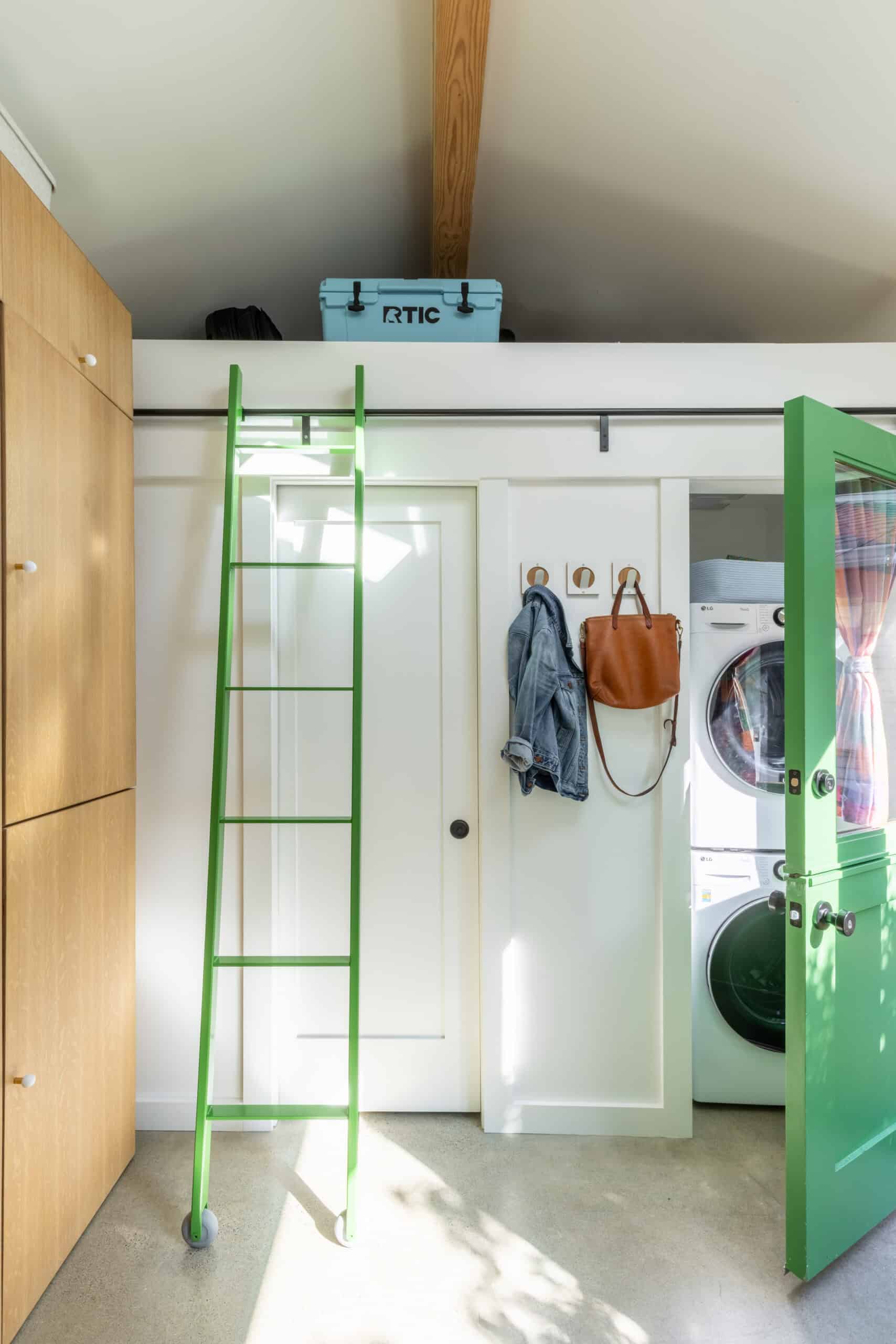 Laundry room with green ladder, washing machine, and storage cabinets.