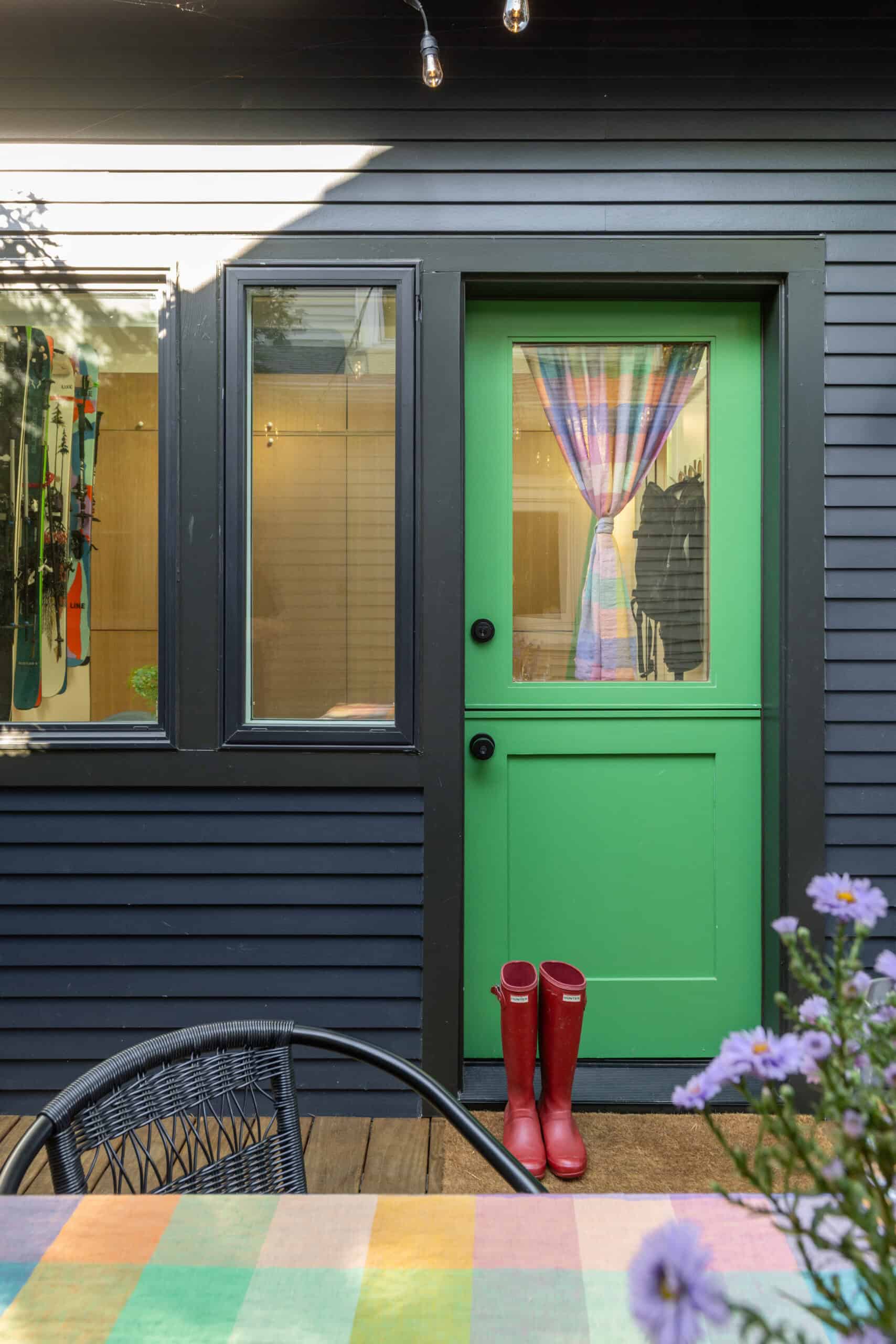 Bright green door with colorful curtain and black siding exterior of a modern building.