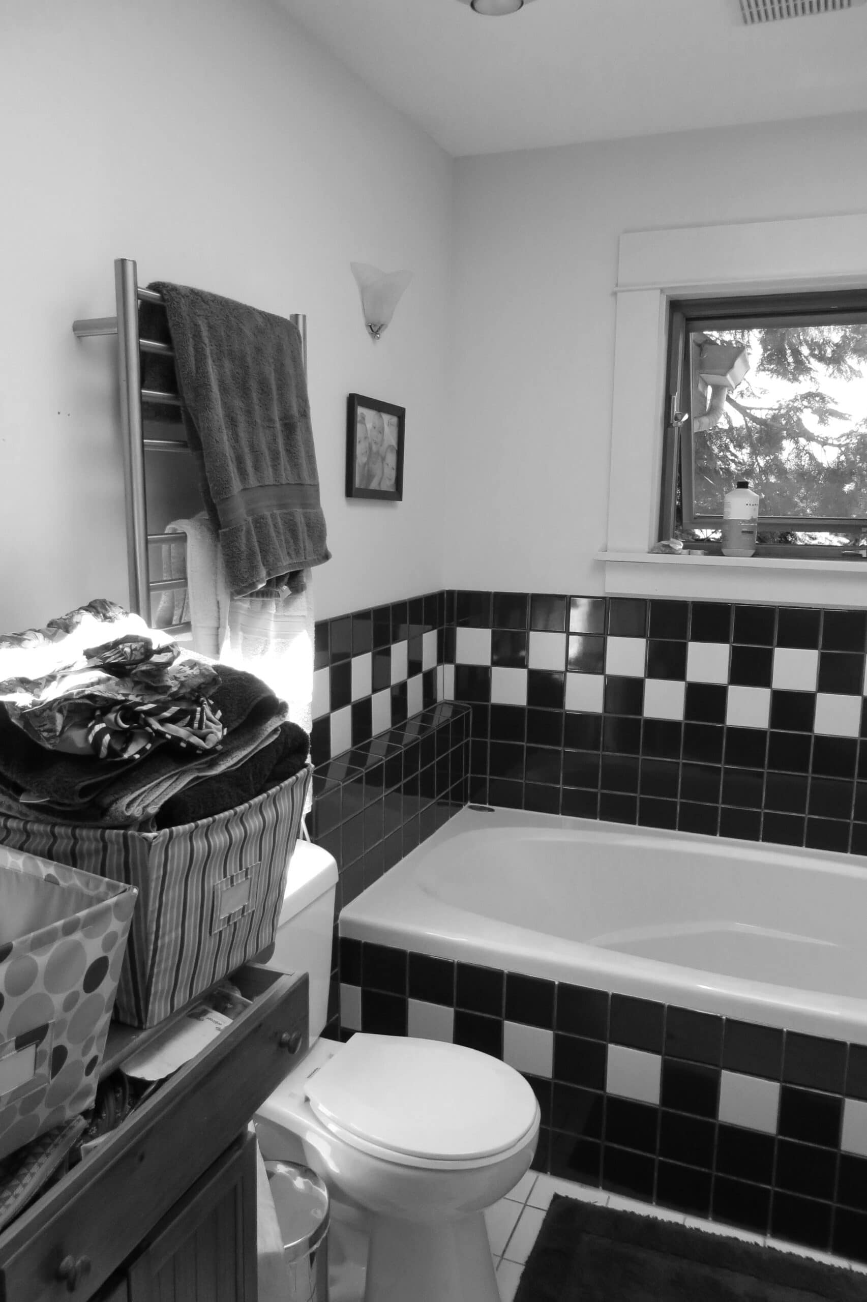 Black and white bathroom with checkered tiles and a bathtub under a window.