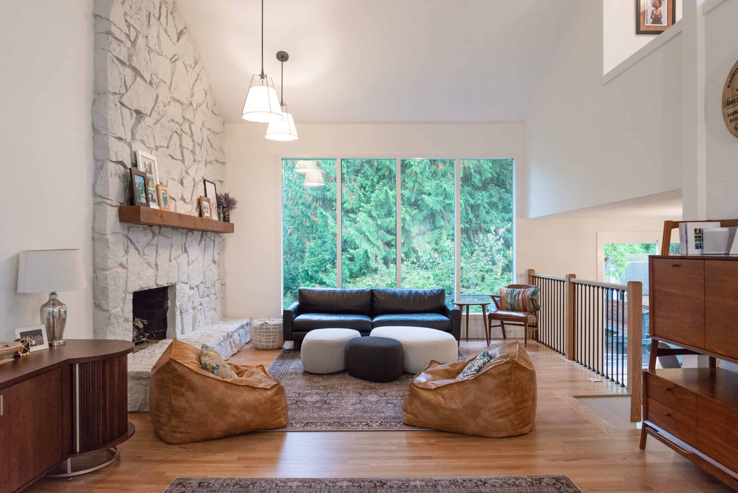 Spacious living room with stone fireplace and large windows overlooking greenery.
