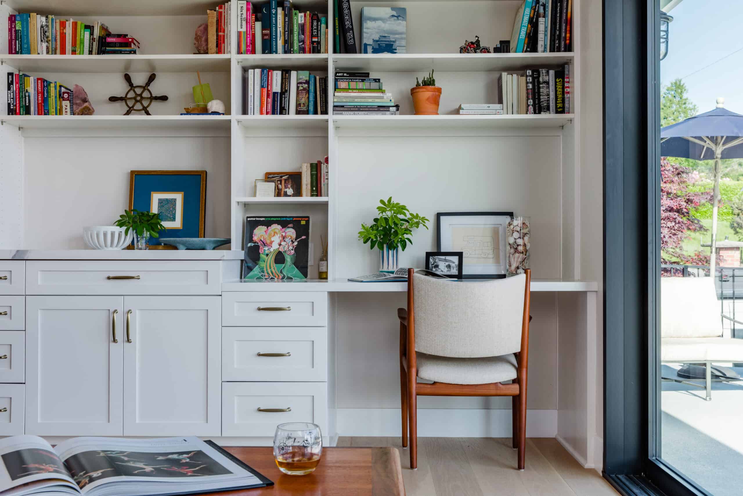Modern home office with white built-in shelves and a cozy reading nook.