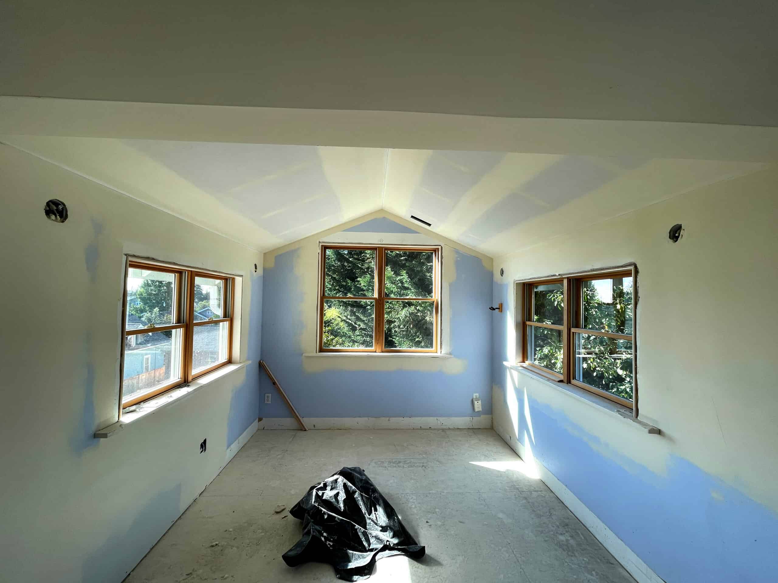 Interior of a room under renovation with three large windows and sloped ceiling.