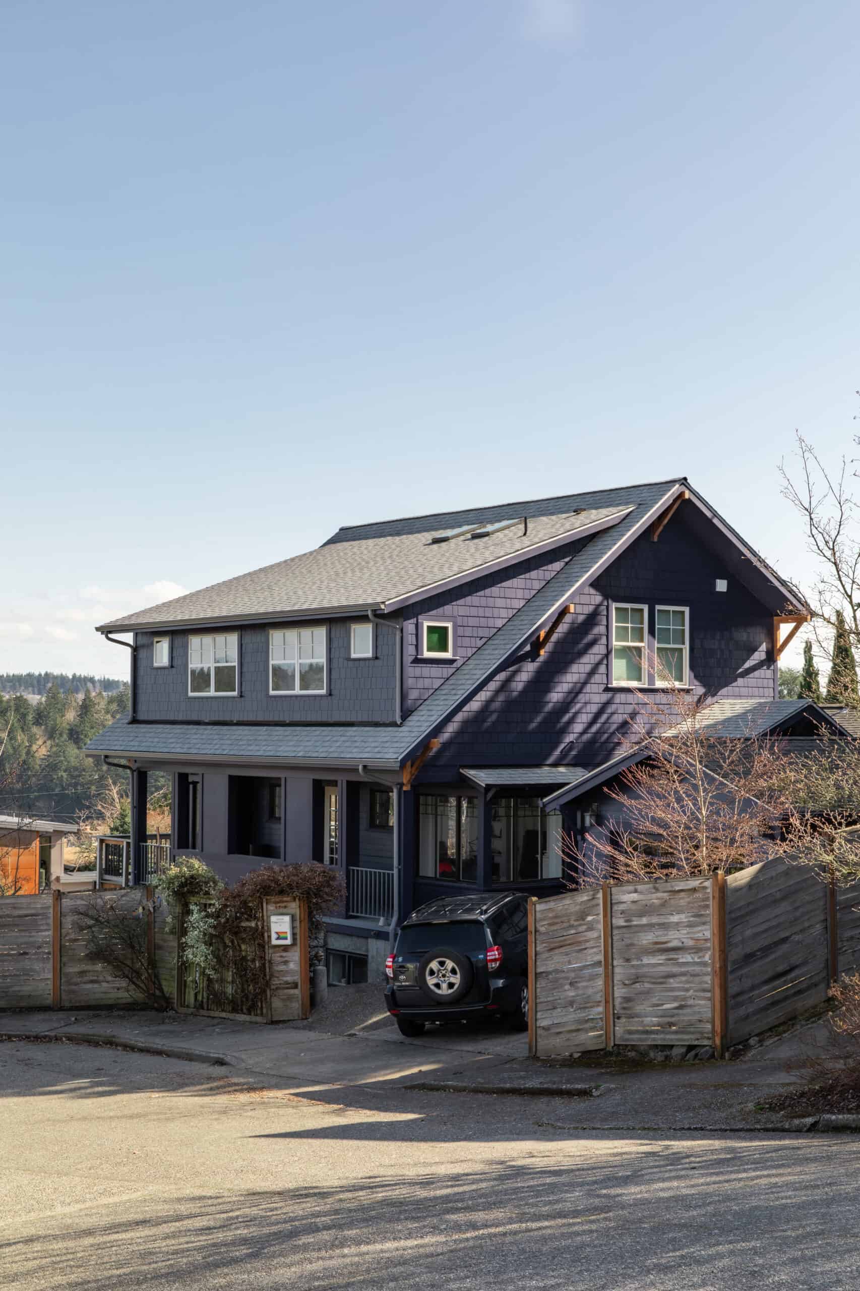 Modern two-story house with dark blue siding and large windows in a suburban neighborhood.