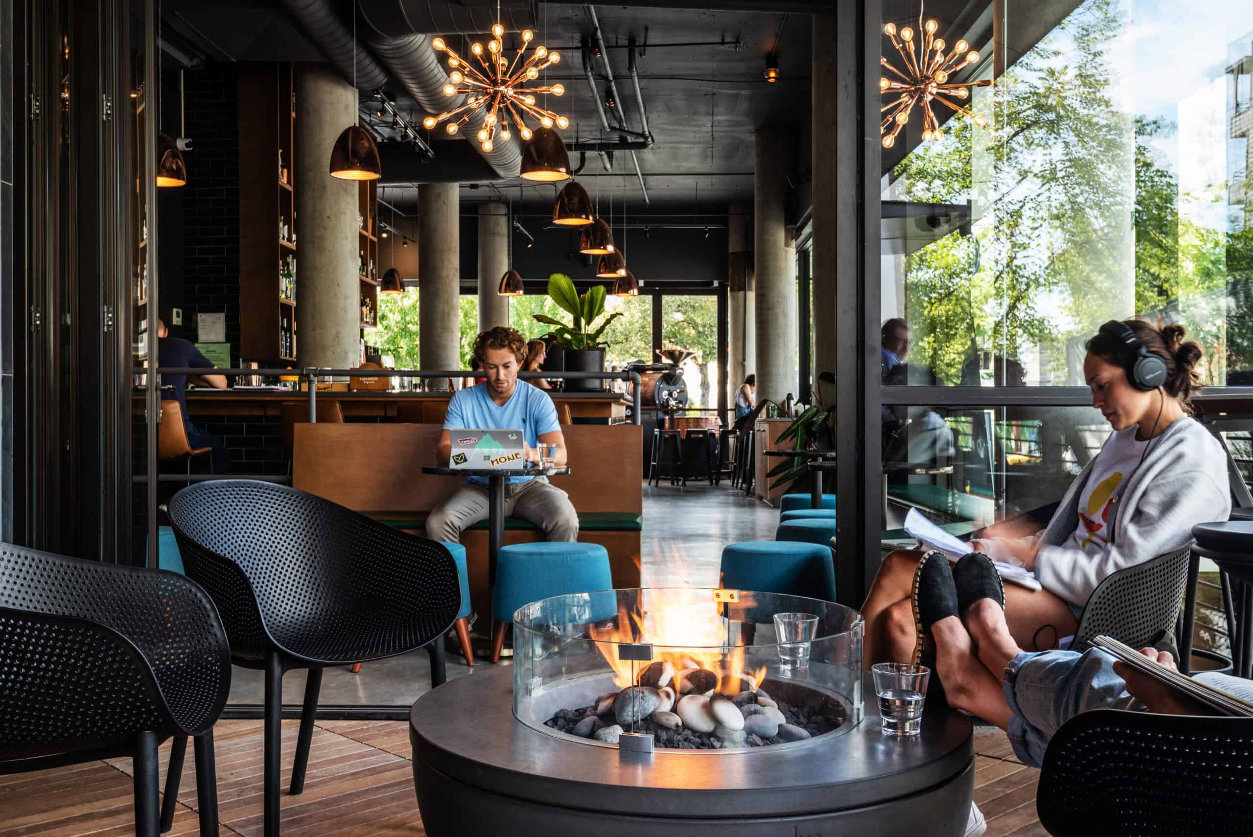 Modern coffee shop interior with seating and fire pit, people working and relaxing.