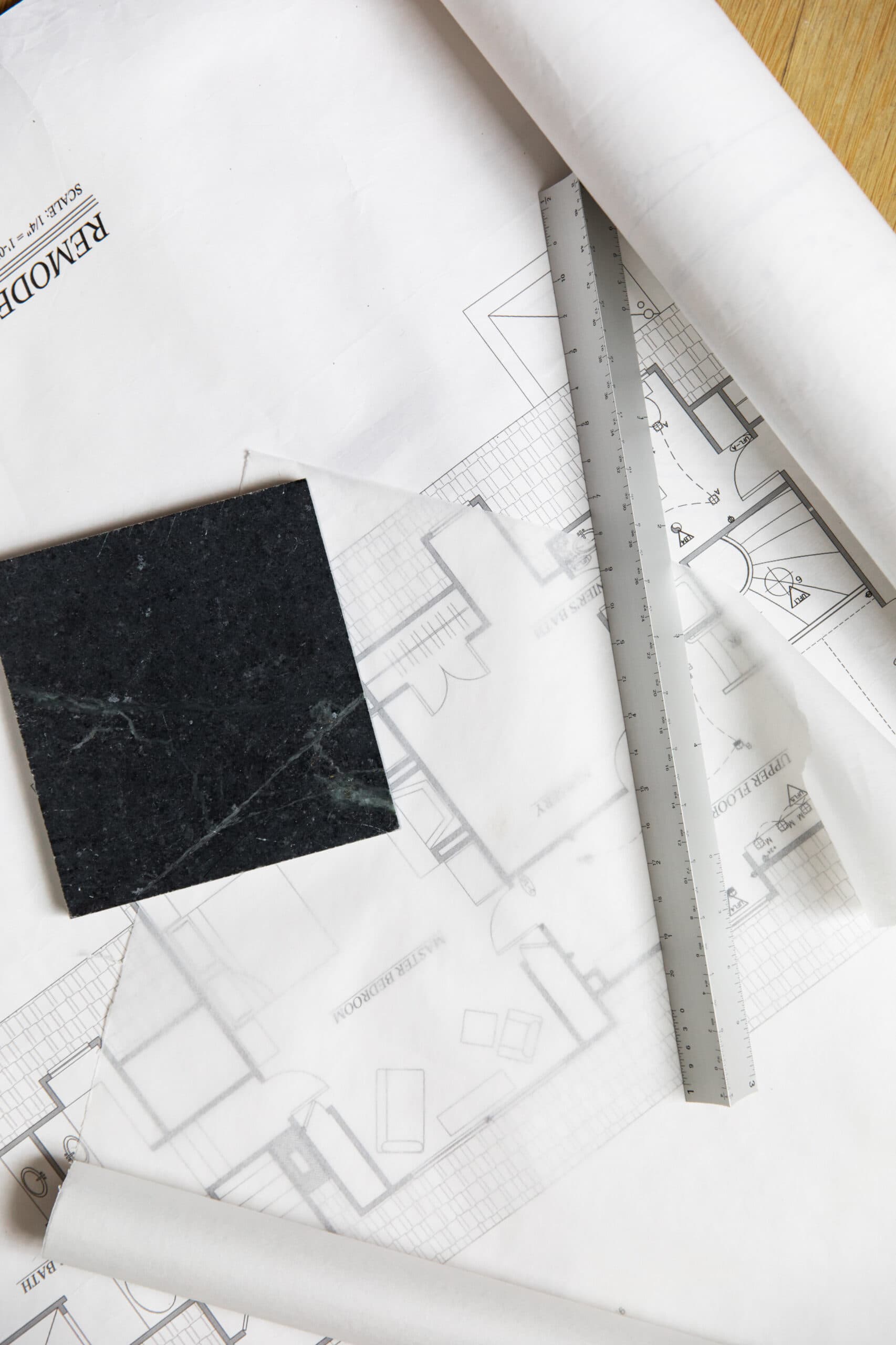 Architectural blueprint with ruler and sample material on wooden desk.