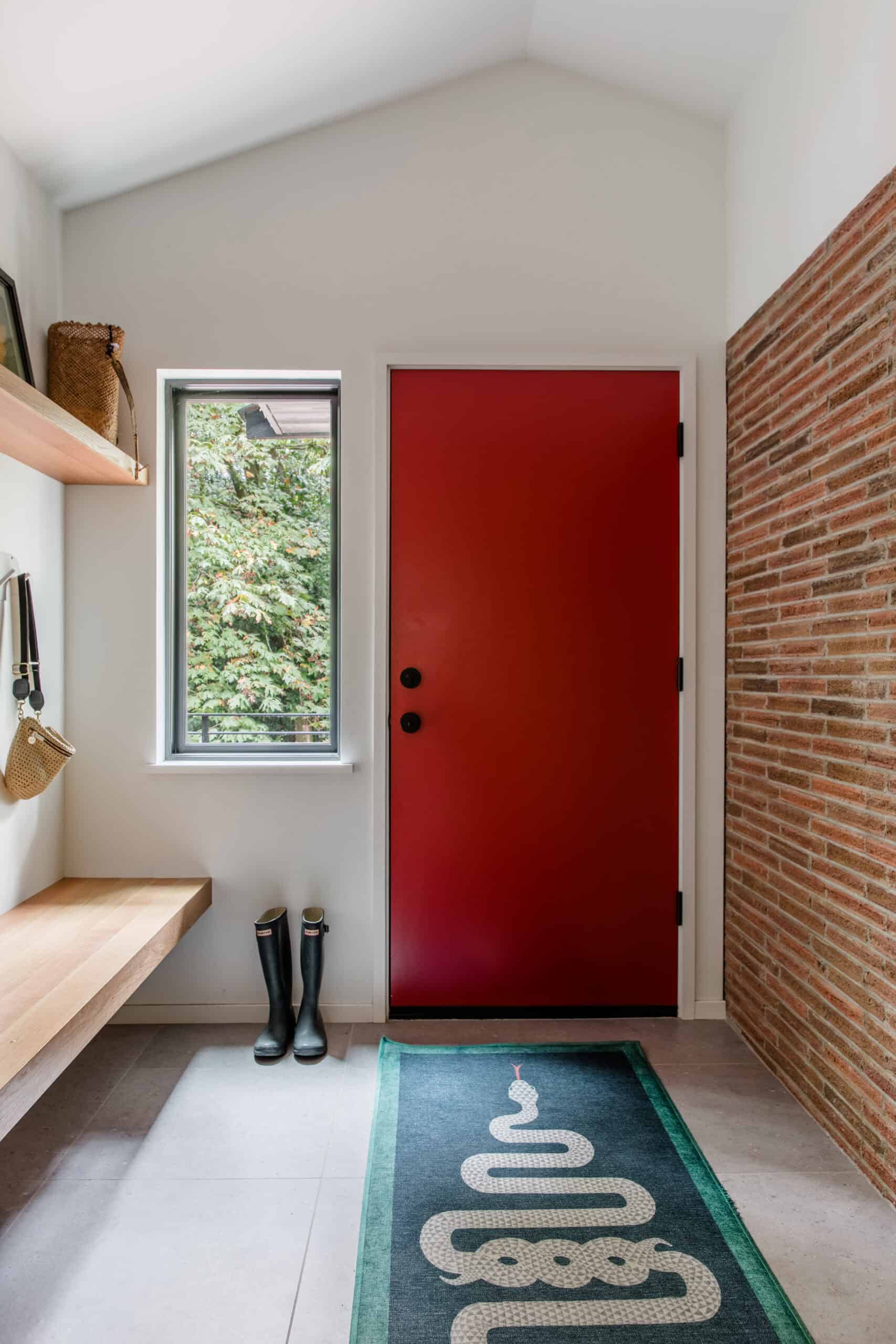 Red front door with black hardware and a small window in a modern home.