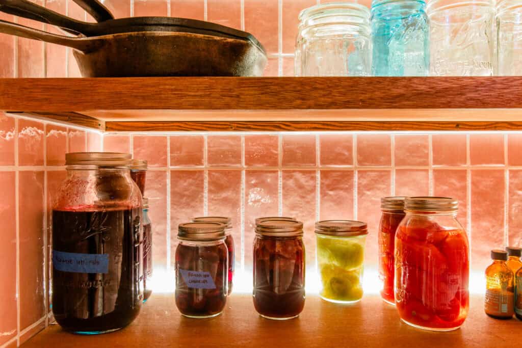 Mason jars filled with colorful preserved foods on kitchen shelf.